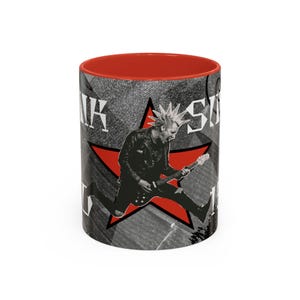 May include: A ceramic mug with a bright red interior and rim. The exterior features a black and white graphic of a person with a mohawk playing an electric guitar, centred over a large red star. The text PUNK SINK is visible in white.