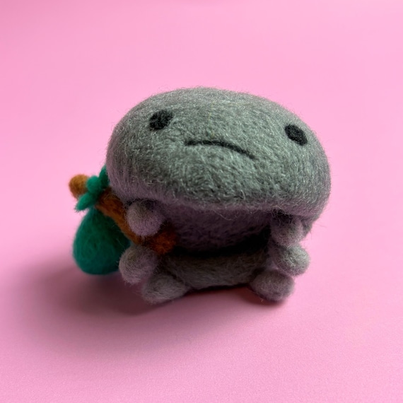 A needle-felted wool roly-poly bug clutching a tiny hobo bindle — absurdly specific, deeply charming, and 100% the work of a real artist's weird brain.