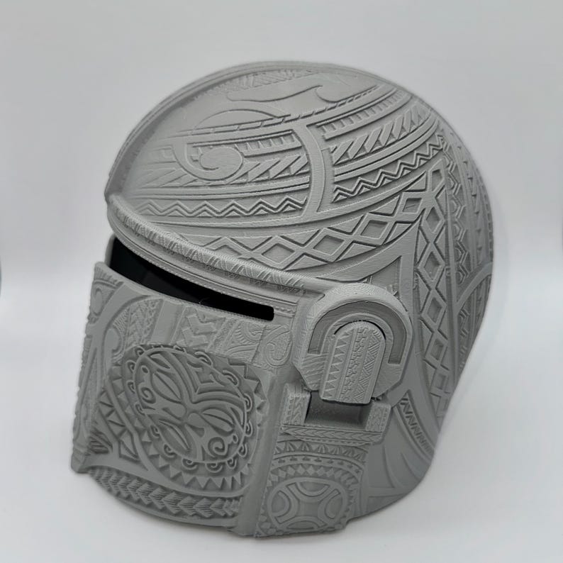 May include: A gray Mandalorian helmet with intricate tribal patterns. The helmet features a visor and detailed relief carvings across the surface, showcasing a blend of geometric and organic designs. The helmet is a solid, three-dimensional object.