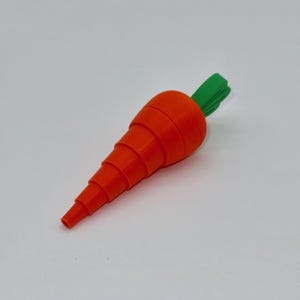 May include: A 3D-printed carrot with a bright orange body and green leafy top. The carrot's body is segmented, with each section decreasing in size towards the tip. The green top has a textured, layered appearance.