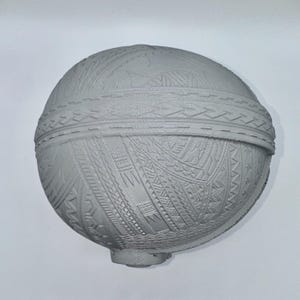 May include: A gray, spherical object with intricate, geometric patterns carved across its surface. The design includes bands of detailed textures and a small, rounded base. The overall aesthetic suggests a handcrafted or ornamental piece.