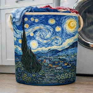 May include: A cylindrical laundry hamper with a blue and yellow embroidered design inspired by Van Gogh's "Starry Night." The hamper features a night sky with swirling stars, a crescent moon, and a village scene. It has beige handles and is filled with clothes.