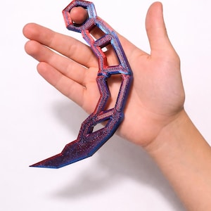 May include: A 3D-printed karambit knife with a geometric design. The knife features a gradient of red and blue colors. The blade is curved with a sharp point. The handle has a series of open hexagonal shapes.