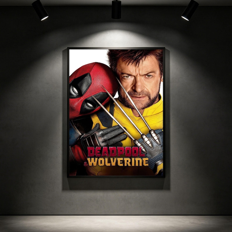 May include: Framed movie poster featuring Deadpool in a red mask and Wolverine with metal claws. The poster has the words "Deadpool & Wolverine" in red and gold. The background is a dark grey wall with spotlights.