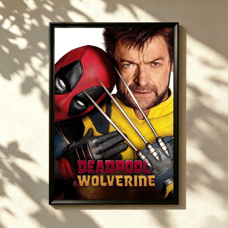 May include: Framed poster featuring Deadpool in a red mask and Wolverine with metal claws. The poster has the words "Deadpool & Wolverine" in red and white text. The characters are set against a yellow and black background.