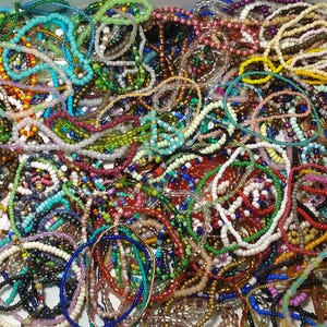 May include: A vibrant assortment of beaded necklaces and bracelets in various colors, including blue, green, red, and yellow. The jewelry pieces are made with small, colorful beads and are intertwined, creating a textured and visually appealing display. The image showcases a variety of styles.