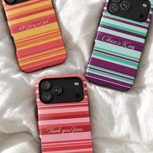 May include: Three smartphone cases featuring horizontal stripes in warm orange and red, cool teal and purple, and shades of pink and red. Each case displays white script text: All Glory to God, Christ is King, and Thank you Jesus respectively.
