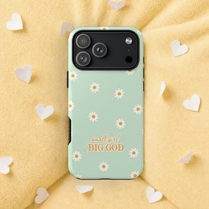 May include: A mint green phone case with a daisy pattern and the text "small girl BIG GOD" in a handwritten style. The case has a black camera module and is surrounded by white paper hearts on a yellow background.