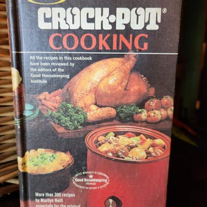 May include: Vintage "Crock-Pot Cooking" cookbook. The cover features a roasted turkey, vegetables, and a red Crock-Pot slow cooker. The book has the text "RIVAL" and "CROCK-POT COOKING" in large letters. The book cover also has the text "Good Housekeeping Institute".