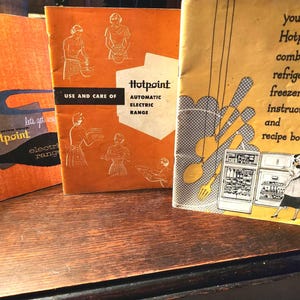 May include: Three vintage Hotpoint appliance manuals. The manuals are orange and yellow with black and white illustrations and text. The titles include "Use and Care of Hotpoint Automatic Electric Range" and "Your Hotpoint Combination Refrigerator-Freezer Instruction and Recipe Book."