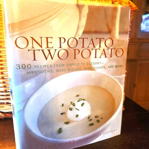 May include: A cookbook titled One Potato Two Potato with 300 recipes from simple to elegant, appetizers, main dishes, side dishes, and more by Roy Finamore with Molly Stevens. The cover features a bowl of creamy soup topped with sour cream and chives.