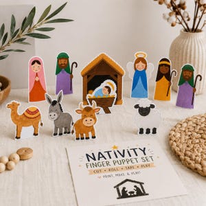 Op de afbeelding: Een kerststal vingerpoppetjesset met papieren uitsparingen van figuren zoals een stal, baby, engel, herders, kameel, ezel, koe en schaap. Een instructiekaart bevat de tekst NATIVITY FINGER PUPPET SET, CUT, ROLL, TAPE, PLAY, PRINT, MAKE & PLAY.