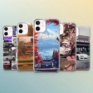 Könnte beinhalten: Eine Sammlung von fünf Handyhüllen mit Designs zum Thema Autos. Die Hüllen zeigen verschiedene Illustrationen, darunter eine Berglandschaft, Kirschblüten und verschiedene Automodelle. Die Hüllen sind transparent mit farbenfrohen Grafiken.