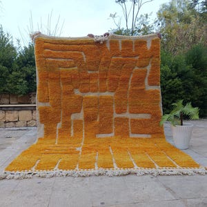 May include: A rectangular area rug featuring a thick, high-pile texture in a vibrant mustard yellow colour. The rug displays a geometric, maze-like pattern created by the contrast between the yellow yarn and the cream-coloured base. It has fringe.