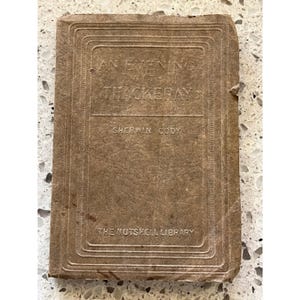 May include: A tan, rectangular, softcover book titled An Evening with Thackeray by Sherwin Cody from The Nutshell Library. The cover features embossed text and a decorative border, showing signs of wear along the edges and corners.