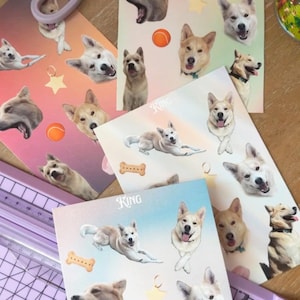 Puede incluir: Hojas de pegatinas con temática de perros con ilustraciones de diferentes razas de perros en varias poses. Las pegatinas incluyen imágenes de perros, huesos, pelotas de tenis y estrellas. También se ven unas tijeras lilas y un cortador de papel.