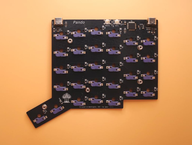 May include: A black printed circuit board for a mechanical keyboard labeled Pando, featuring numerous purple switch sockets, two USB-C ports at the top, and a small tree logo. The board includes various electronic components and surface-mounted parts.