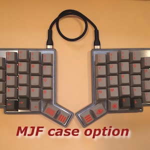 May include: A split ergonomic mechanical keyboard with grey keycaps and red legends. The keyboard features a single red keycap on the left side, a black connecting cable, and a metallic frame. The text MJF case option is printed below the keyboard.