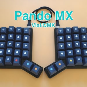 May include: A split ergonomic mechanical keyboard labeled Pando MX Vial/QMK with dark blue keycaps. The keys feature small, centered circular accents in white, orange, red, green, purple, yellow, and light blue. A black cable connects the two halves.