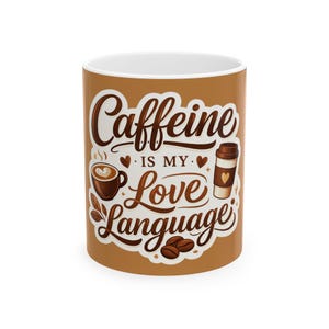 May include: A ceramic coffee mug with a brown exterior and white interior. The mug features the text "Caffeine is my Love Language" in a decorative font, along with coffee-related illustrations, including a coffee cup, a to-go cup, and coffee beans.