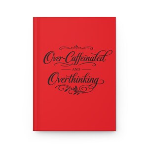 Op de afbeelding: Een rood notitieboek met de zwarte tekst "Over-Caffeinated and Overthinking". Het ontwerp van het notitieboek is eenvoudig en elegant, ideaal voor het maken van notities of persoonlijke dagboeken.