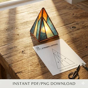 Pode incluir: Uma lanterna de vitral em forma de pirâmide com painéis laranja, azuis e amarelos. A lanterna está sobre uma mesa de madeira ao lado de uma folha de padrão com a etiqueta "Pyramid Lantern". O texto "INSTANT PDF/PNG DOWNLOAD" está na parte inferior.