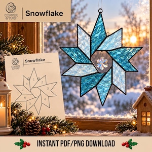 May include: A star-shaped stained glass ornament featuring textured blue and clear glass panels with black metal soldering. A small, clear, faceted crystal snowflake charm hangs from the center. A paper pattern labeled Snowflake is visible.