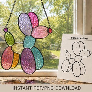 May include: A colorful stained glass balloon animal in the shape of a dog hangs in front of a window. The dog is made of various colors, including pink, purple, green, and yellow. A paper with the text "Balloon Animal" and a diagram is next to the dog.