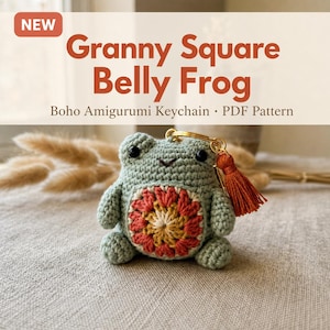 Könnte beinhalten: Ein gehäkelter salbeigrüner Frosch-Schlüsselanhänger mit einem bauchigen Granny-Square-Muster in Rost, Gelb und Creme. Der Frosch hat schwarze Perlenaugen, einen kleinen gestickten Mund und einen goldfarbenen Metallring mit einer rostfarbenen Stoffquaste.