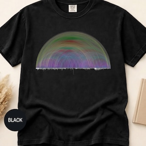 Puede incluir: Una camiseta negra de manga corta con un estampado gráfico de un diseño de arco semicircular compuesto por líneas finas superpuestas en tonos verde, azul y morado, situado sobre una línea horizontal de barras verticales blancas.