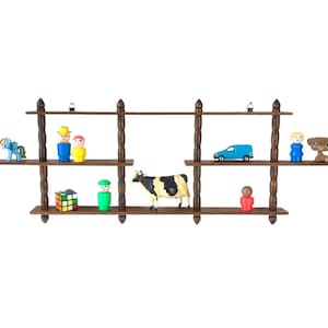 May include: A dark brown wooden shelf unit with three shelves, displaying various toys. The toys include a blue toy car, a cow figurine, and several small plastic figures. The shelves are supported by decorative posts.