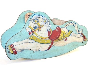 Pode incluir: Um cavalo de baloiço de madeira vintage pintado num esquema de cores azul claro, branco, vermelho e amarelo. O cavalo está deitado com a cabeça virada para o lado. O cavalo tem uma sela e uma rédea.