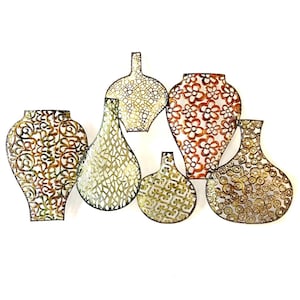 Op de afbeelding: Een set van zes metalen wandsculpturen in de vorm van vazen. De vazen zijn versierd met ingewikkelde uitgesneden ontwerpen en hebben een gouden en bruine afwerking.