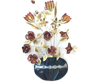 Pode incluir: Uma escultura de parede de metal de um vaso com flores. O vaso é azul escuro com detalhes dourados e as flores são vermelhas e douradas.
