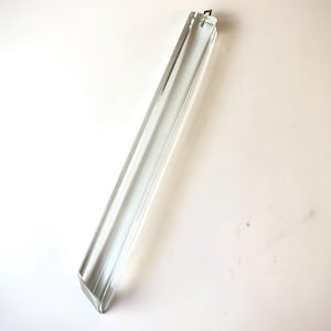 Può includere: Un tubo di vetro trasparente e rettangolare con un'estremità leggermente angolata. Il tubo è trasparente, permettendo alla luce di passare attraverso. L'oggetto è posizionato diagonalmente su uno sfondo bianco.