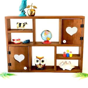May include: A wooden shelf unit with multiple compartments and decorative items. Includes a turquoise owl figurine, a gold apple, a cow figurine, a globe, and a variety of other small objects. The unit has two doors with heart-shaped cutouts.
