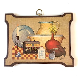 Puede incluir: Arte decorativo de pared con una composición de naturaleza muerta. La obra representa una vela, platos, una jarra, un jarrón con flores, un cofre y una botella. La paleta de colores incluye beige, rojo, amarillo y azul. El marco tiene un borde marrón oscuro.