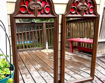 Pode incluir: Dois espelhos retangulares combinando com a parte superior arqueada. As molduras são marrons escuras com entalhes ornamentados e detalhes em vermelho. Os espelhos são exibidos ao ar livre em um deck de madeira.