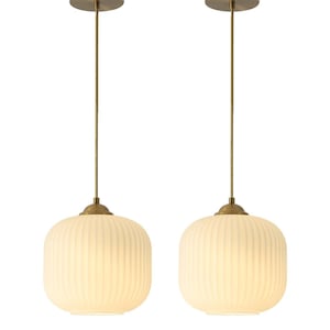 May include: Two pendant lights with a brass finish. Each light has a round, ribbed, off-white glass shade. The lights hang from a brass canopy and a brass rod.
