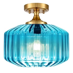 May include: A semi-flush mount ceiling light fixture featuring a vibrant, ribbed turquoise glass shade with a cylindrical shape. The fixture is supported by a circular, brushed brass metal canopy and a central stem, showcasing a clear light bulb.