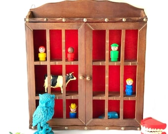 Pode incluir: Uma vitrine de madeira vintage com interior vermelho, contendo várias figuras de brinquedo e uma figura de vaca. Uma estátua de coruja turquesa e um conjunto de dentes de brinquedo também estão presentes.