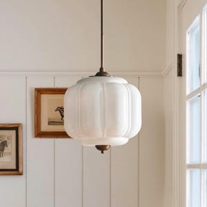 May include: A white, ribbed, spherical glass pendant light fixture suspended from a thin, dark metal rod. The light features decorative, dark-toned metal hardware at the top and bottom, connecting the glass shade to the central mounting stem.