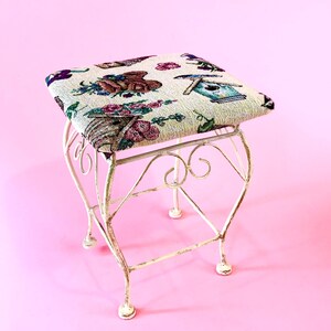 May include: A white metal stool with a floral patterned fabric seat. The stool has a delicate, ornate design and is perfect for a small space.