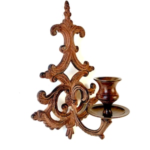 May include: Ornate metal wall sconce with a single candle holder. The sconce is brown and has a decorative design.