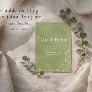Peut inclure: Un modèle de faire-part de mariage vert avec les noms "Mia & Ethan" en texte blanc. L'invitation comprend les détails de la date et du lieu du mariage. L'invitation est entourée de branches d'eucalyptus et repose sur un tissu beige.