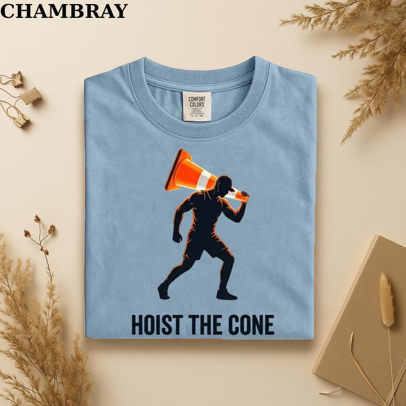 May include: Light blue t-shirt with a graphic of a person carrying an orange traffic cone. The text "HOIST THE CONE" is printed below the graphic. The shirt has a crew neck and a Comfort Colors tag.