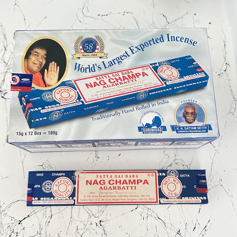 May include: A box and a stick of Satya Sai Baba Nag Champa incense. The box is blue and white with text and images, including a portrait and the words "World's Largest Exported Incense." The incense stick is blue and white.