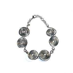 May include: A silver-toned bracelet featuring multiple spiral-shaped wire designs. The bracelet is connected by small chain links and has a clasp closure. The spirals are evenly spaced and create a unique, artistic look.