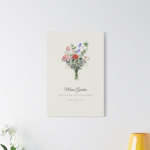 Printify room context showing a personalized Birth Flower Family Bouquet Canvas above a neutral sofa. The 16x20 inch stretched canvas combines watercolor birth month flowers, family names and the title Mom's Garden in a warm botanical arrangement. This ready to hang family canvas art is shown at home as a Christmas gift for mom or grandma, Mother's Day present or housewarming keepsake.