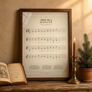 Away in a Manger vintage hymnal print in a rustic walnut frame leaning on an antique console, an open vintage hymnal book beside it, a brass candlestick with beeswax candle, a sprig of holly and a dried orange slice, warm golden light. Cottage Christmas faith home decor, single Luke 2:7 hymn print digital download TheFramedVerse.
